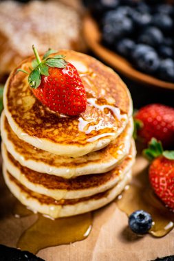 A pile of pancakes with berries and honey. On a black background. High quality photo