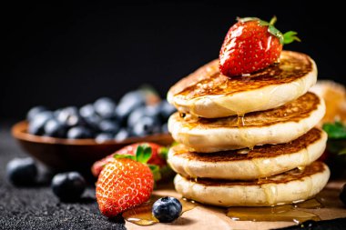 A pile of pancakes with berries and honey. On a black background. High quality photo