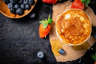 A pile of pancakes with berries and honey. On a black background. High quality photo