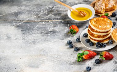 Pancakes in a plate with berries and honey. On a gray background. High quality photo