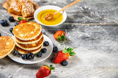 Pancakes in a plate with berries and honey. On a gray background. High quality photo