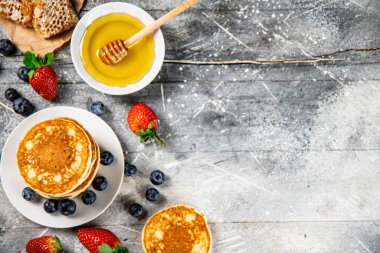 Pancakes in a plate with berries and honey. On a gray background. High quality photo