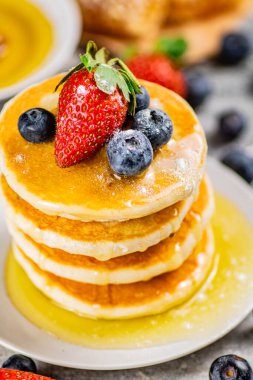 Pancakes with honey and berries on a plate. On a gray background. High quality photo