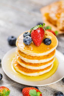 Pancakes with honey and berries on a plate. On a gray background. High quality photo