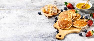 Homemade pancakes on a cutting board with honey and berries. On a gray background. High quality photo