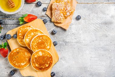 Homemade pancakes on a cutting board with honey and berries. On a gray background. High quality photo