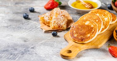 Homemade pancakes on a cutting board with honey and berries. On a gray background. High quality photo