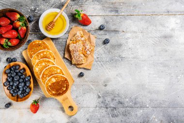 Homemade pancakes on a cutting board with honey and berries. On a gray background. High quality photo