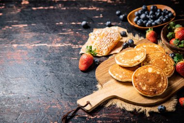 Pancakes on a wooden cutting board with honey and berries. Against a dark background. High quality photo
