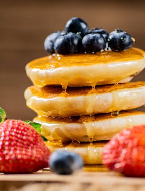 A pile of pancakes with fresh berries and honey on the table. On a wooden background. High quality photo