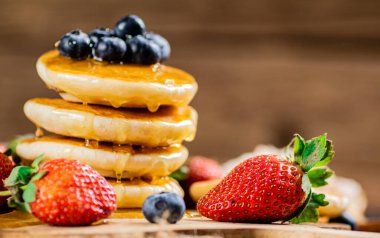 A pile of pancakes with fresh berries and honey on the table. On a wooden background. High quality photo