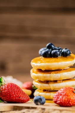 A pile of pancakes with fresh berries and honey on the table. On a wooden background. High quality photo