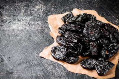 A bunch of delicious prunes on paper on the table. On a black background. High quality photo