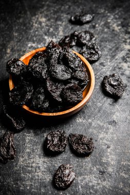 Prunes in a wooden plate on the table. On a black background. High quality photo