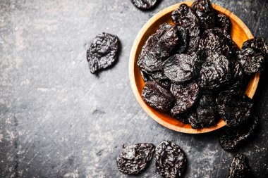Prunes in a wooden plate on the table. On a black background. High quality photo