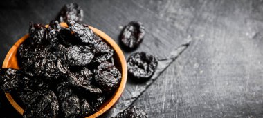 Prunes in a wooden plate on a stone board. On a black background. High quality photo