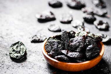 Prunes in a wooden plate on the table. On a black background. High quality photo