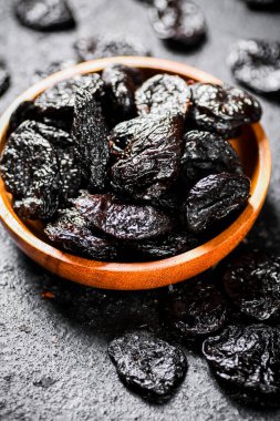 Prunes in a wooden plate on the table. On a black background. High quality photo