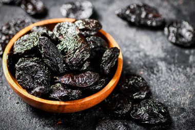 Prunes in a wooden plate on the table. On a black background. High quality photo