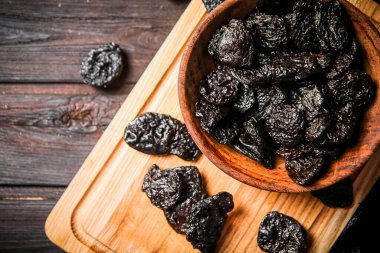 Prunes on a wooden cutting board. On a dark wooden background. High quality photo