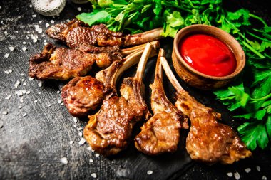 Rack of lamb with tomato sauce and parsley on the table. On a black background. High quality photo