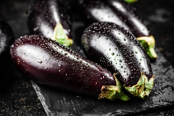 Fresh ripe eggplant with droplets of water on a stone board. On a black background. High quality photo