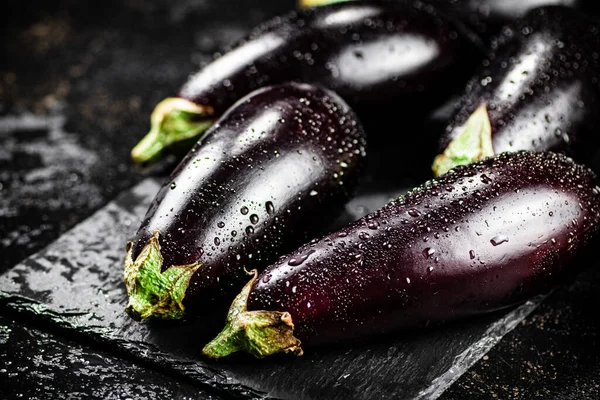 Fresh ripe eggplant with droplets of water on a stone board. On a black background. High quality photo