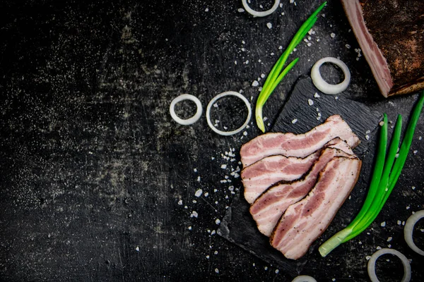 stock image Delicious lard on a stone board with onions and spices. On a black background. High quality photo