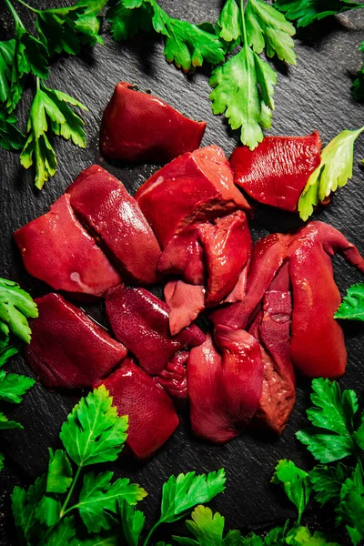 stock image Pieces of raw liver on a stone tray with parsley. On a black background. High quality photo