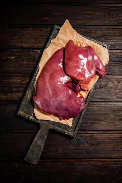 Raw liver on a cutting board on paper. On a wooden background. High quality photo