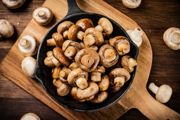 stock image Fried mushrooms in a frying pan on a cutting board. On a wooden background. High quality photo