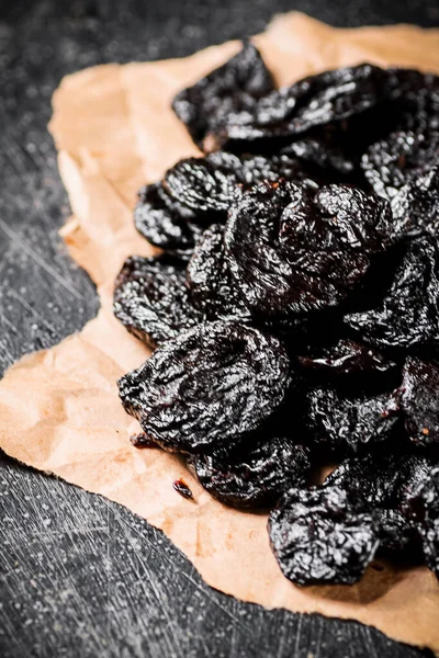 A bunch of delicious prunes on paper on the table. On a black background. High quality photo