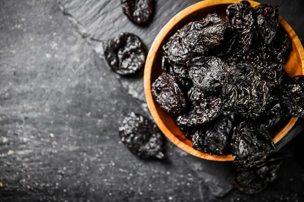 stock image Prunes in a wooden plate on a stone board. On a black background. High quality photo