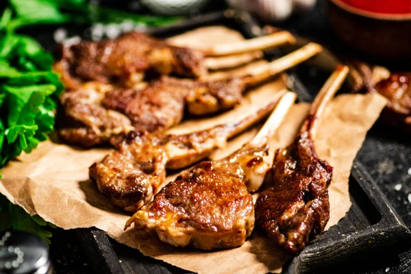 Grilled lamb rack on a cutting board with herbs and tomato sauce. On a black background. High quality photo