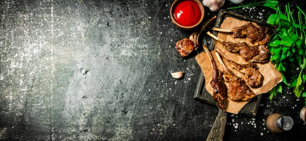 stock image Grilled lamb rack on a cutting board with herbs and tomato sauce. On a black background. High quality photo