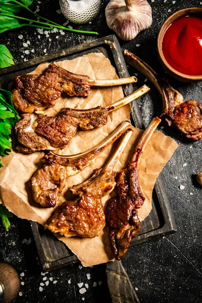 Grilled lamb rack on a cutting board with herbs and tomato sauce. On a black background. High quality photo