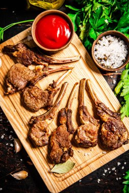 Grilled rack of lamb on a cutting board with parsley and tomato sauce. Against a dark background. 