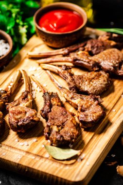 Grilled rack of lamb on a cutting board with parsley and tomato sauce. Against a dark background. 