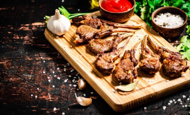 Grilled rack of lamb on a cutting board with parsley and tomato sauce. Against a dark background. 