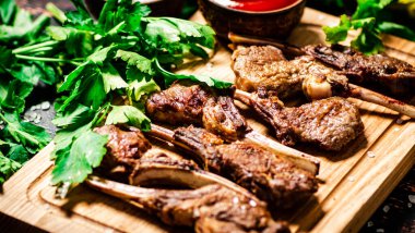 Grilled rack of lamb on a cutting board with parsley and tomato sauce. Against a dark background. 