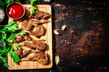 Grilled rack of lamb on a cutting board with parsley and tomato sauce. Against a dark background. 