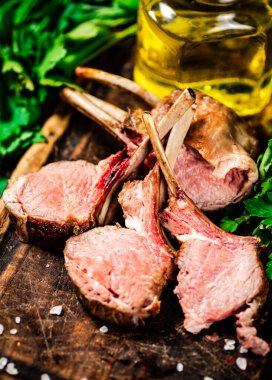 Rack of grilled lamb on a wooden cutting board with parsley. Against a dark background. 