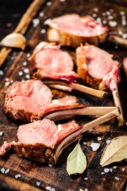 Rack grilled lamb on a cutting board with bay leaves. Against a dark background. 