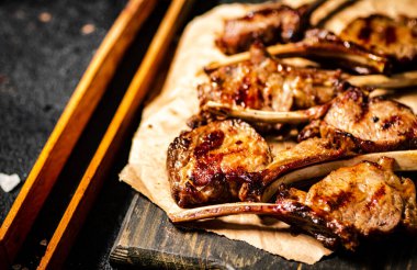 A rack of grilled lamb on a cutting board on paper. On a black background. High quality photo
