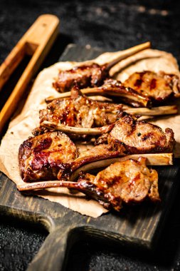 A rack of grilled lamb on a cutting board on paper. On a black background. High quality photo