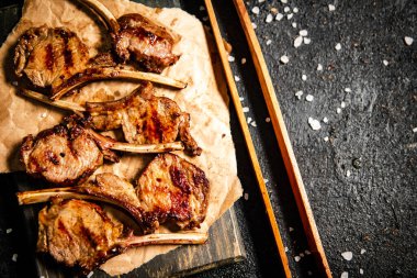 A rack of grilled lamb on a cutting board on paper. On a black background. High quality photo