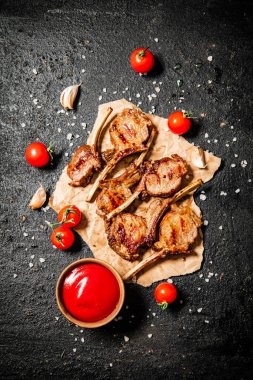 Grilled lamb rack on paper with tomato sauce and cherry tomatoes. On a black background. High quality photo