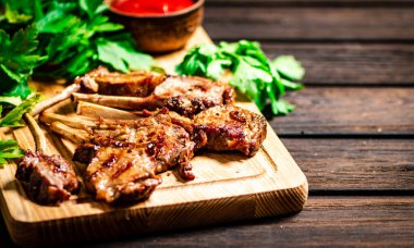 Grilled rack lamb on a cutting board with tomato sauce and parsley. On a wooden background. 