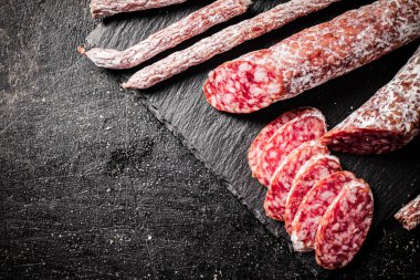 Pieces of salami sausage on a stone board. On a black background. High quality photo