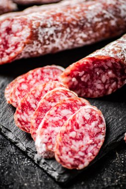 Pieces of salami sausage on a stone board. On a black background. High quality photo